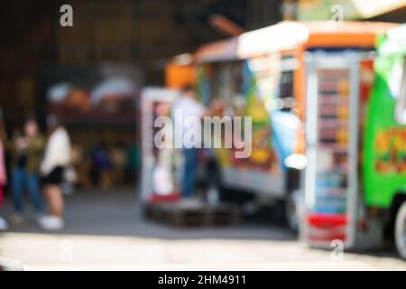 Abstrakt verschwommener Hintergrund von Food Trucks. Menschen, die Lebensmittel in einem Foodtruck kaufen Stockfoto