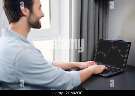 Freier Mitarbeiter analysiert Aktienmarktdaten, Indexdiagramm für Handelsdaten auf dem Laptop-Bildschirm, Rückansicht. Qualifizierter Händler Mann verdienen online, investieren in Kryptowährung Stockfoto