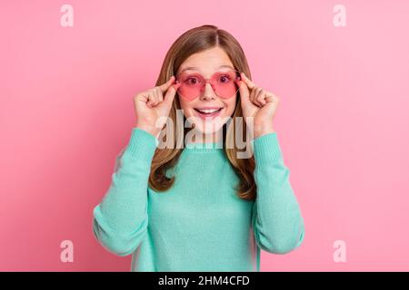 Foto von beeindruckt Schulmädchen gekleidet teal Pullover Arme Herz Brille isoliert rosa Farbe Hintergrund Stockfoto