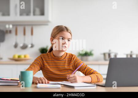 Serious kaukasischen Teenager-Mädchen blond sitzt am Tisch, schaut auf Laptop, Studien in minimalistischen Küche Stockfoto