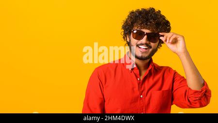 Porträt eines bärtigen, gutaussehenden Mannes mit schwarzer Brille im lässigen Stil, der die Kamera anschaut und modisch lächelt. Studio auf orangefarbenem Hintergrund aufgenommen Stockfoto