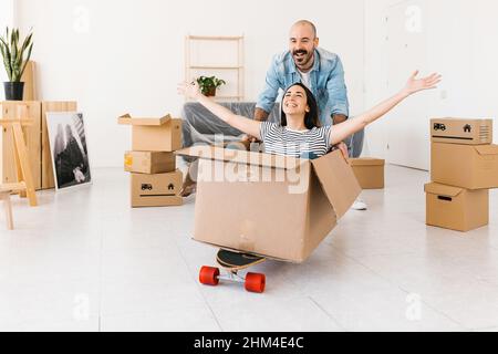 Glückliches Paar, das Spaß beim Auspacken am Umzugstag in einer neuen Wohnung hat Stockfoto