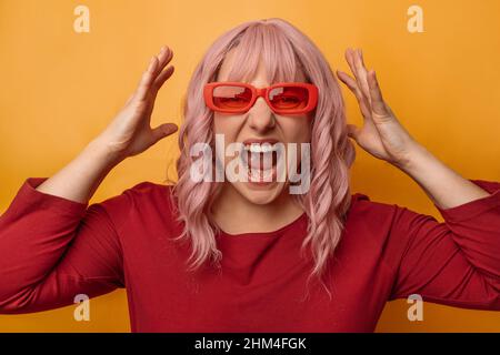 Gestresste emotionale verärgerte 30s Frau, die mit der Hand auf dem Kopf wegen Schmerzen im Kopf steht und über vereinzelten gelben Hintergrund schreit. Migräne leiden. Gesundheit Stockfoto