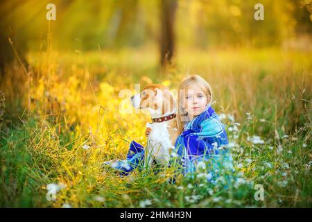 Das süße Mädchen geht bei Sonnenuntergang mit ihrem Beagle-Welpen in einen Park, sitzt hinter einer karierten Decke und umarmt einen Hund, beste Freundin Stockfoto