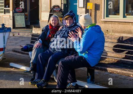 Die Diskussion. Drei Personen saßen auf einer Bank an der Hafenfront und genossen die letzte der untergehenden Wintersonne, während sie die Welt in Ordnung gebracht haben. Stockfoto