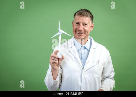 Wissenschaftler mit weißer Schicht hält die Miniatur-Windenergieanlage vor grünem Hintergrund Stockfoto