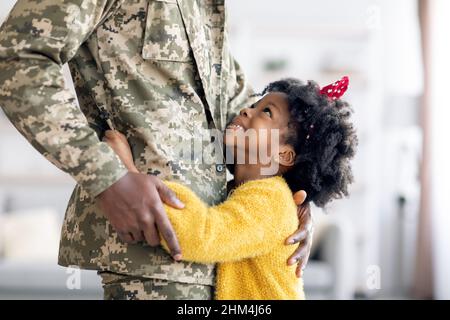 Happy Little Black Tochter Umarmt Soldat Vater In Militäruniform Zu Hause Stockfoto