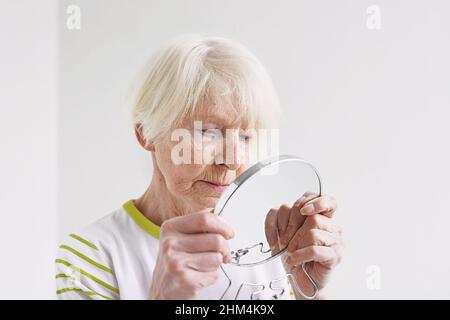 Ältere traurige Frau, die sich im Spiegel ansieht. Alter, Zeit, Hautpflegekonzept Stockfoto