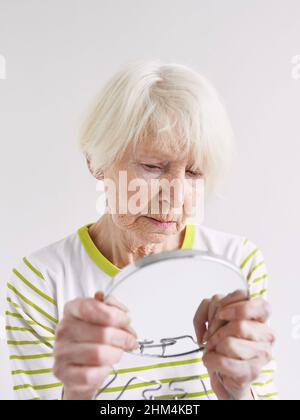 Ältere traurige Frau, die sich im Spiegel ansieht. Alter, Zeit, Hautpflegekonzept Stockfoto