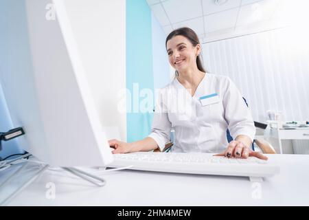 Lächelnd erfreut fokussierte Ärztin, die in ihrem Büro arbeitet Stockfoto