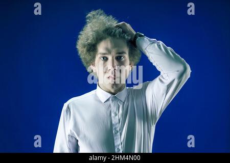 Frustration und Frustration Konzept. Frustrierter Mann mit lockigen Haaren blickt traurig in die Kamera und hält seine Haare mit einer Hand. Stockfoto