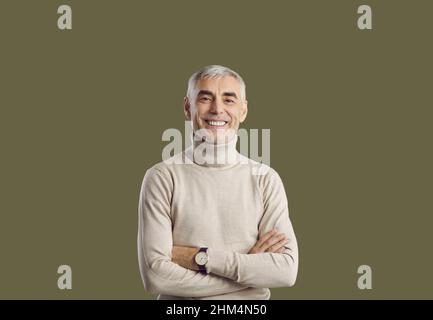 Glücklicher, lächelnder älterer Mann mit gefalteten Armen, isoliert auf grünem Hintergrund stehend Stockfoto