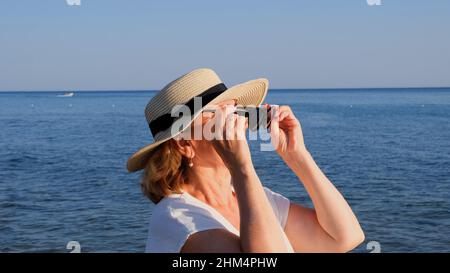 Porträt einer reifen Frau im Alter von 50 Jahren mit Strohhut und Sonnenbrille vor blauem Meeresgrund. Sommer, Urlaub, Urlaub, aktive Rentner Stockfoto