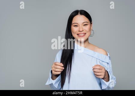 Glücklich asiatische Modell in Bluse Blick auf Kamera isoliert auf grau Stockfoto