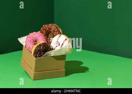 Donuts in Bastelkiste rosa, chocolate und weiß auf grünem conner-Papier-Hintergrund Stockfoto