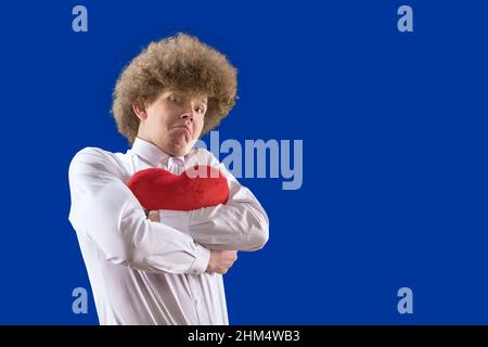 Liebe. Ein Geschenk für deinen Seelenverwandten. Liebhaber. Ein Mann mit lockigen Haaren hält ein herzförmiges weiches Spielzeug in seinen Händen. Der 14th. februar. Valentinstag. Stockfoto