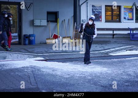 Eine Frau mit Corona-Maske trägt ihren Schlitten und überquert die Eisenbahnstrecke am Bahnhof Eibsee auf der Zugspitze. Stockfoto