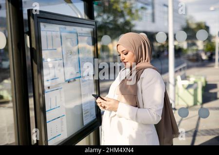 Frau benutzt Handy an der Bushaltestelle Stockfoto