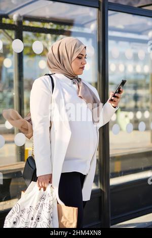 Frau benutzt Handy an der Bushaltestelle Stockfoto