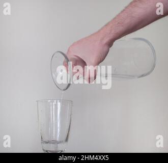 Gießt die letzten Tropfen Wasser von Hand aus einem Glaskrug in ein Glas Stockfoto