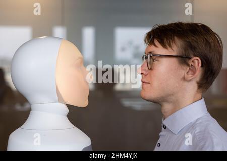 Junger Mann, der den Sprachassistenten des Roboters ansieht Stockfoto