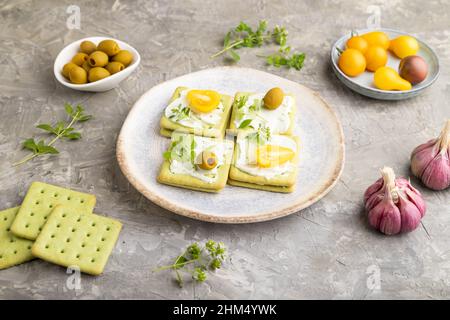 Green Cracker Sandwiches mit Frischkäse und Kirschtomaten auf grauem Beton-Hintergrund. Seitenansicht, Nahaufnahme. Stockfoto