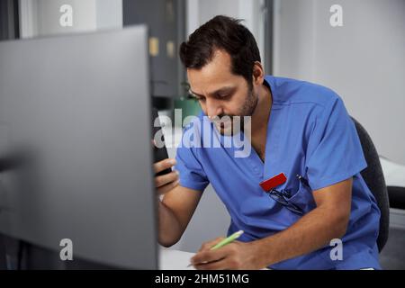 Männlicher Arzt mit Smartphone im Büro Stockfoto