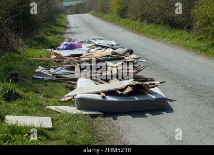 Nahsicht auf Haushaltsmüll, einschließlich einer Matratze, die achtlos über eine schmale Landstraße abgeführt wird und eine Fahrgefahr darstellt. Stockfoto