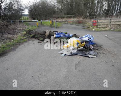 Gartenabfälle in Form von Turves, Erde, Plastiktüten und Filzfliege, die durch einen öffentlichen Fußweg in die Landschaft gekippt werden Stockfoto