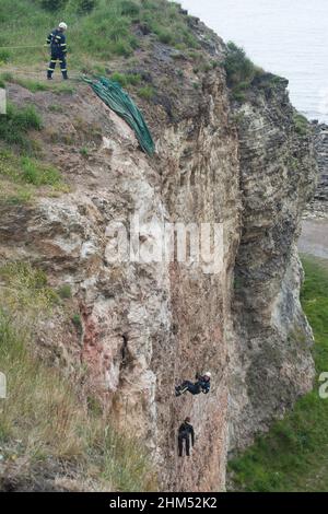 Lange Sicht der Feuerwehrmänner bei der Trainingsübung Abseilen an der Felswand in der Scheinrettung der Figur, die in diesem Fall ein Dummy ist Stockfoto