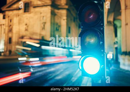 Grün auf Ampel gegen Straßenbahn und Autos in unscharfen Bewegungen. Nachtszene der Straße in Prag, Tschechische Republik. Stockfoto