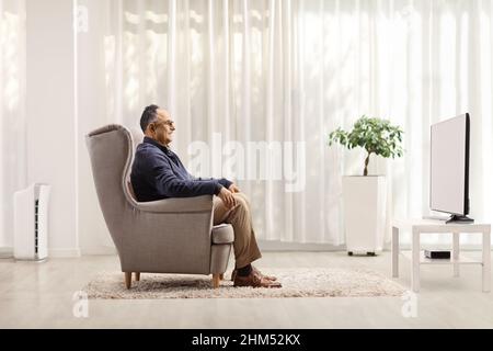 Profilaufnahme eines reifen Mannes, der in einem Sessel sitzt und zu Hause Fernsehen sieht Stockfoto