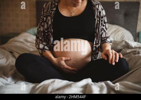 Eine Schwangerin sitzt auf dem Bett und berührt den Bauch Stockfoto