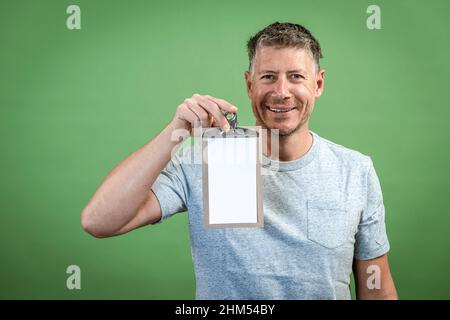 Mann mit grauem Hemd hält Clipboard vor grünem Hintergrund Stockfoto