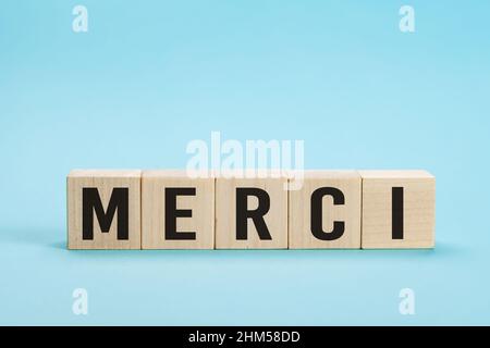 Merci - Danke in französischer Sprache. Merci Wort auf Buchstabenfliesen auf blauem Hintergrund. Minimale Ästhetik. Wort merci danke auf französisch auf Holz Stockfoto