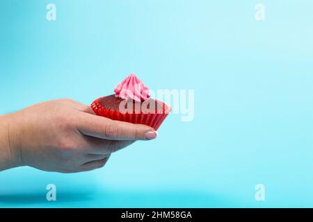 Hand hält Cupcake mit rosa Belag auf blauem Hintergrund mit Kopierraum. Stockfoto