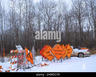 Orangefarbene Straßenwarnschilder stehen im Winterschnee, in der Nähe eines Pilot Car Pickups Stockfoto