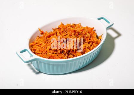 Reisjollof in einem Gericht auf weißem Hintergrund. Traditionelle nigrische Gerichte aus Reis, Tomaten und Gewürzen. Stockfoto