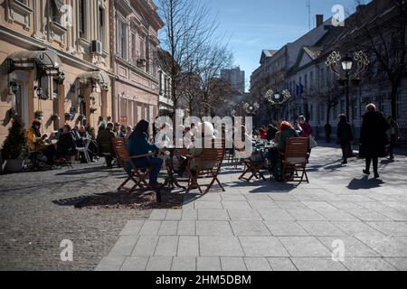 Belgrad, Serbien, 6. Feb 2022: Blick auf ein überfülltes Straßencafé in Zemun, in dem sitzende Gäste die Wintersonne genießen Stockfoto