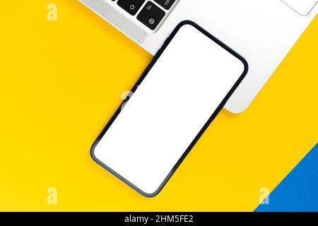 Modell von oben. Smartphone mit leerem weißen Bildschirm, flacher gelber Hintergrund mit Laptop. Minimaler Arbeitsplatz, moderner Laptop, Kopierplatz Stockfoto