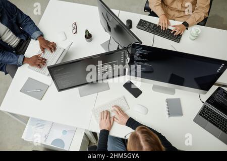 Hände von jungen interkulturellen Softwareentwicklern, die auf Computertastaturen tippen, während sie an Schreibtischen im Büro oder im Büro sitzen Stockfoto