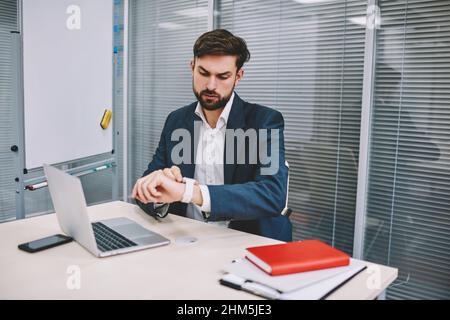 Ein seriöser Geschäftsmann, der im Büro auf eine Armbanduhr schaut Stockfoto