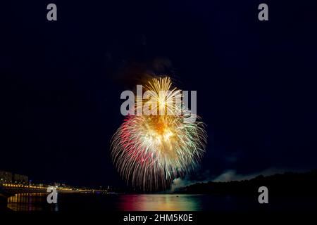 Festliches Feuerwerk über dem Fluss einer Großstadt. Zentraler Volley. Stockfoto