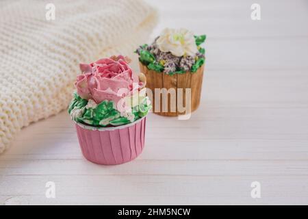 Zwei Muffins mit bunten Butterblumen auf weißem Holztisch mit hellgrünem Hintergrund. Hygge-Stil Stockfoto