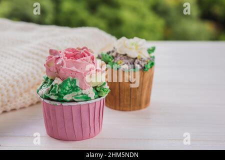 Zwei Muffins mit bunten Butterblumen auf weißem Holztisch mit hellgrünem Hintergrund. Hygge-Stil Stockfoto