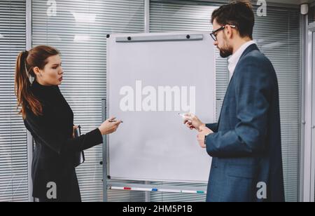 Kollegen stehen in der Nähe des Whiteboards und diskutieren das Projekt Stockfoto