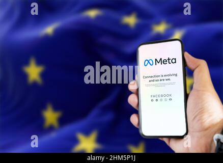 Rom, Italien, 2022. Februar: Hand hält ein Telefon mit der mobilen Meta-App auf dem Bildschirm und die winkende Flagge der Europäischen Union verschwimmt im Hintergrund. Meta Stockfoto