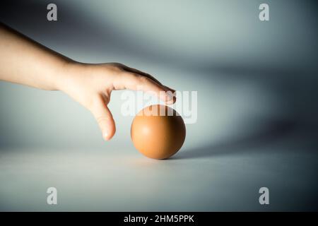 Einzelnes braunes Ei isoliert von weißem Hintergrund. Die Hand des Kindes greift nach dem Ei. Konzept. Nahaufnahme Stockfoto