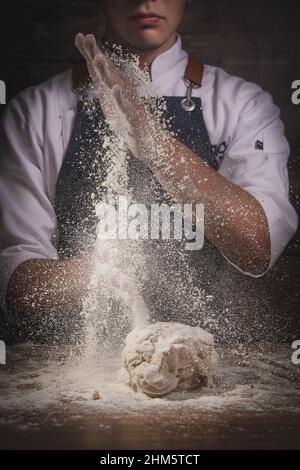 Schöner junger Mann Koch kocht Brot auf einem Holztisch und Holzhintergrund Stockfoto