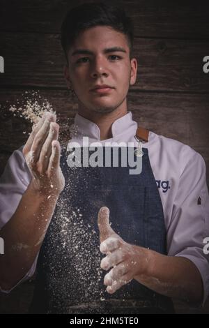 Schöner junger Mann Koch kocht Brot auf einem Holztisch und Holzhintergrund Stockfoto